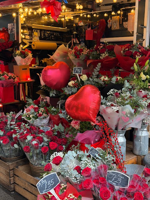 A display of vibrant floral arrangements at the flowerscrystalpalace.co.uk shop, featuring red roses, white lilies, and greenery in various bouquets and containers. Among the flowers, there are large